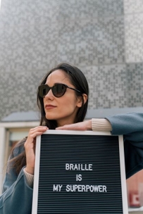 Woman holding a sign saying "Braille is My Superpower"