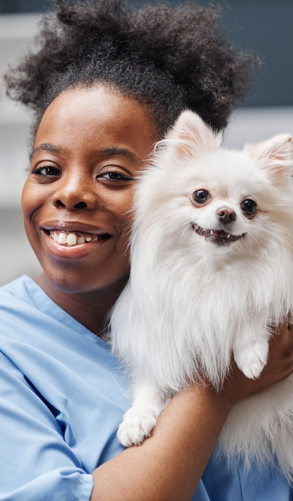 Veterinary professional smiling while holding a small white dog